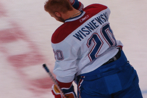 Ein Eishockeyspieler in einem "Wisniewski"-Trikot steht auf dem Eis und hölt einen Eishockeyschläger mit konzentrierter und entschlossener Miene.