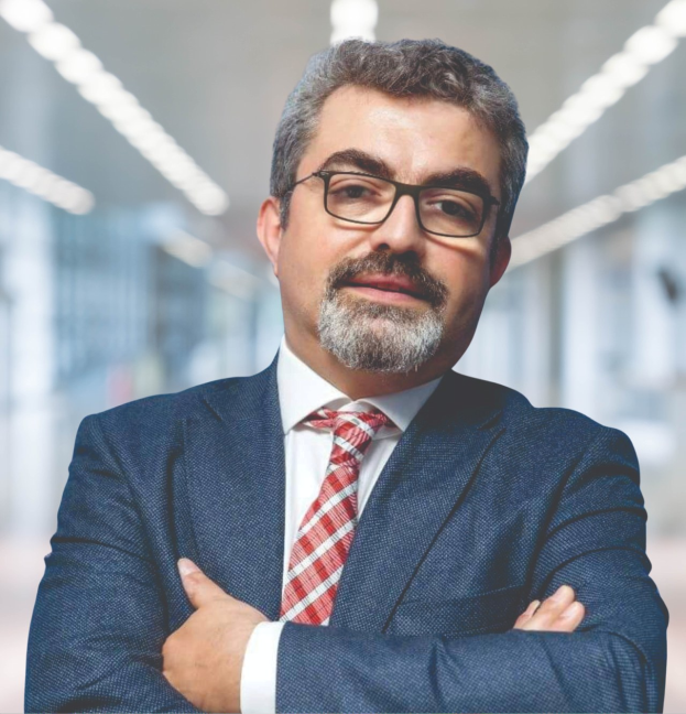 Ein Mann im Anzug und mit Krawatte, der die Arme verschränkt und eine Brille trägt, vor einem unscharfen Hintergrund steht, identifiziert als der neu ernannte Marketingchef durch Text unten.