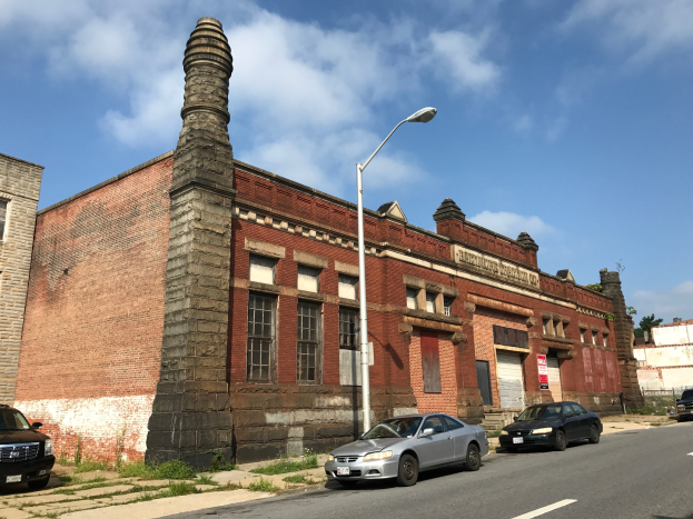 Ein Ziegelgebäude mit seitlichem Schornstein, identifiziert als die ehemalige St. Louis Feuerwache, umgeben von Straßenmasten, Laternen, Fahrzeugen, Schildern, Bäumen und einem bewölkten Himmel.