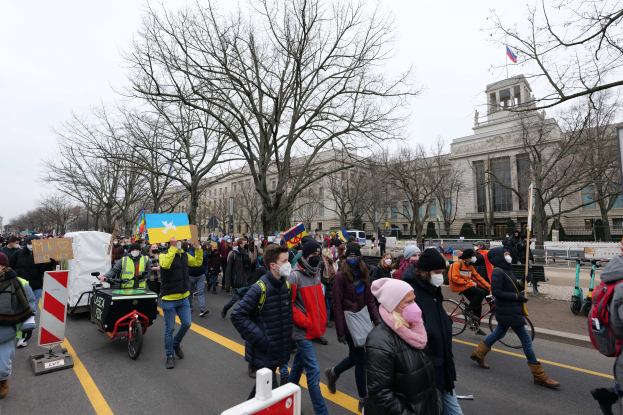Großer Protestmarsch in Washington, D.C. am 21. Januar 2020, mit Menschen, die Plakate halten und Fahrräder fahren, vor einem Gebäude auf einer Straße unter einem klaren blauen Himmel.