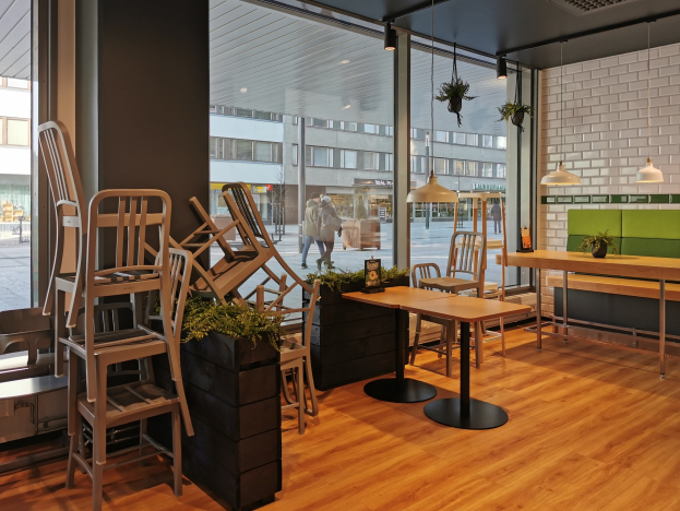 Ein Berliner Restaurant mit Holztischen und -stühlen vor einem großen Fenster, das eine Außenansicht von Fußgängern, Gebäuden und städtischen Elementen zeigt.