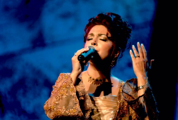 Frau in goldenem Kleid, die in ein Mikrofon singt, vor blau-schwarzem Hintergrund bei der Eurovision.