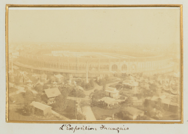 Altes Schwarz-Weiß-Foto eines Stadions in städtischer Umgebung mit umliegenden Gebäuden, Bäumen und Strommasten; unten ist Text sichtbar.