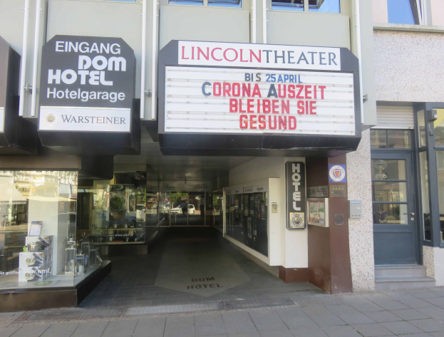 Außenansicht des Lincoln Theaters in Berlin, Deutschland, mit Glasfenstern und -türen, einem Textschild und einer belebten Stadtlandschaft im Inneren.
