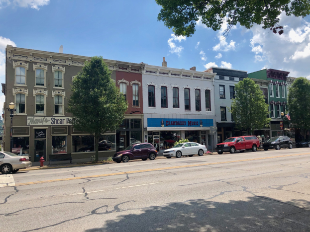 Stadtstraße mit parkenden Autos, Gebäuden, Bäumen, Laternen, einem Hydranten und einem bewölkten Himmel, mit zwei Immobilienanzeigetafeln, auf denen "Crawford, NC Immobilienanzeige" steht.