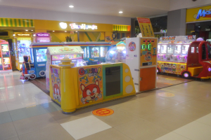 Ein geräumiger Arcade-Raum mit verschiedenen Arten von Arcade-Automaten, Deckenleuchten und einer Hintergrundwand, der eine Vergnügungspark-Atmosphäre schafft.