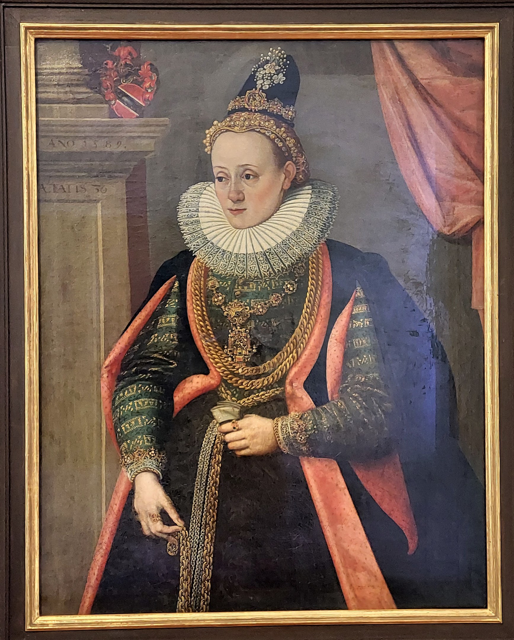 Porträt der Queen Elizabeth I. von England in königlicher Kleidung mit einer Krone und Tiara, ihr Haar zu einem Knoten gebunden, seitlich blickend mit einem würdevollen Gesichtsausdruck, gerahmt an einer Wand.