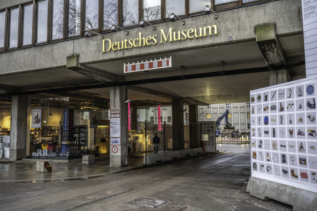 Großes modernes Gebäude mit Glasfenstern und Säulen, beschriftet mit "Deutsches Museum" in Berlin, Deutschland, mit Informationsschildern und umgebender Stadtlandschaft.