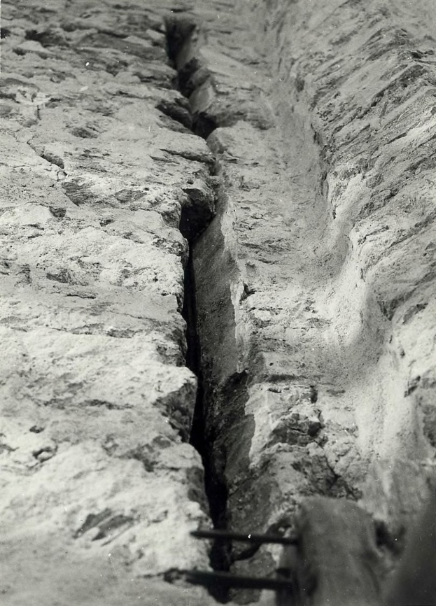Schwarzes und weißes Foto eines großen Risses im Boden, wahrscheinlich ein Entwässerungsgraben, mit einem sichtbaren Wasserzeichen auf der linken Seite.