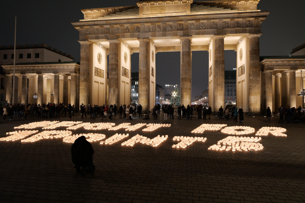 Eine Gruppe von Menschen steht vor dem beleuchteten Reichstag in Berlin, Deutschland, umgeben von Gebäuden, Mästen und Lichtern, und die Worte 'Kampf für die Freiheit' sind auf den Boden geschrieben.