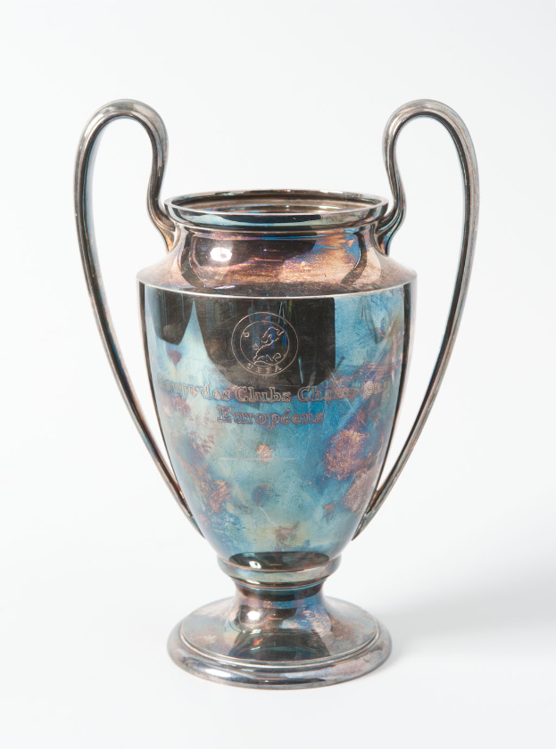 Der UEFA-Champions-League-Pokal, ein stählerner Becher mit zwei Griffen und einem blauen und silbernen Farbschema, mit der Inschrift "UEFA Champions League" auf einem weißen Hintergrund.