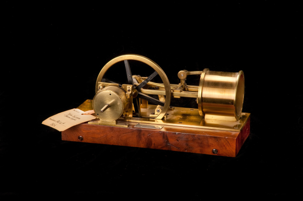 Altmodische Uhr mit einem hölzernen Sockel, Metallrad und einem Papier-Zeitschalter, vor einem schwarzen Hintergrund.