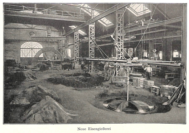 Altes Schwarz-Weiß-Foto einer Fabrik mit Arbeitern, die Maschinen bedienen, umgeben von Metallstangen und -pfählen, beschriftet mit "Neue Eisengießerei, die erste Fabrik in Deutschland" unten.