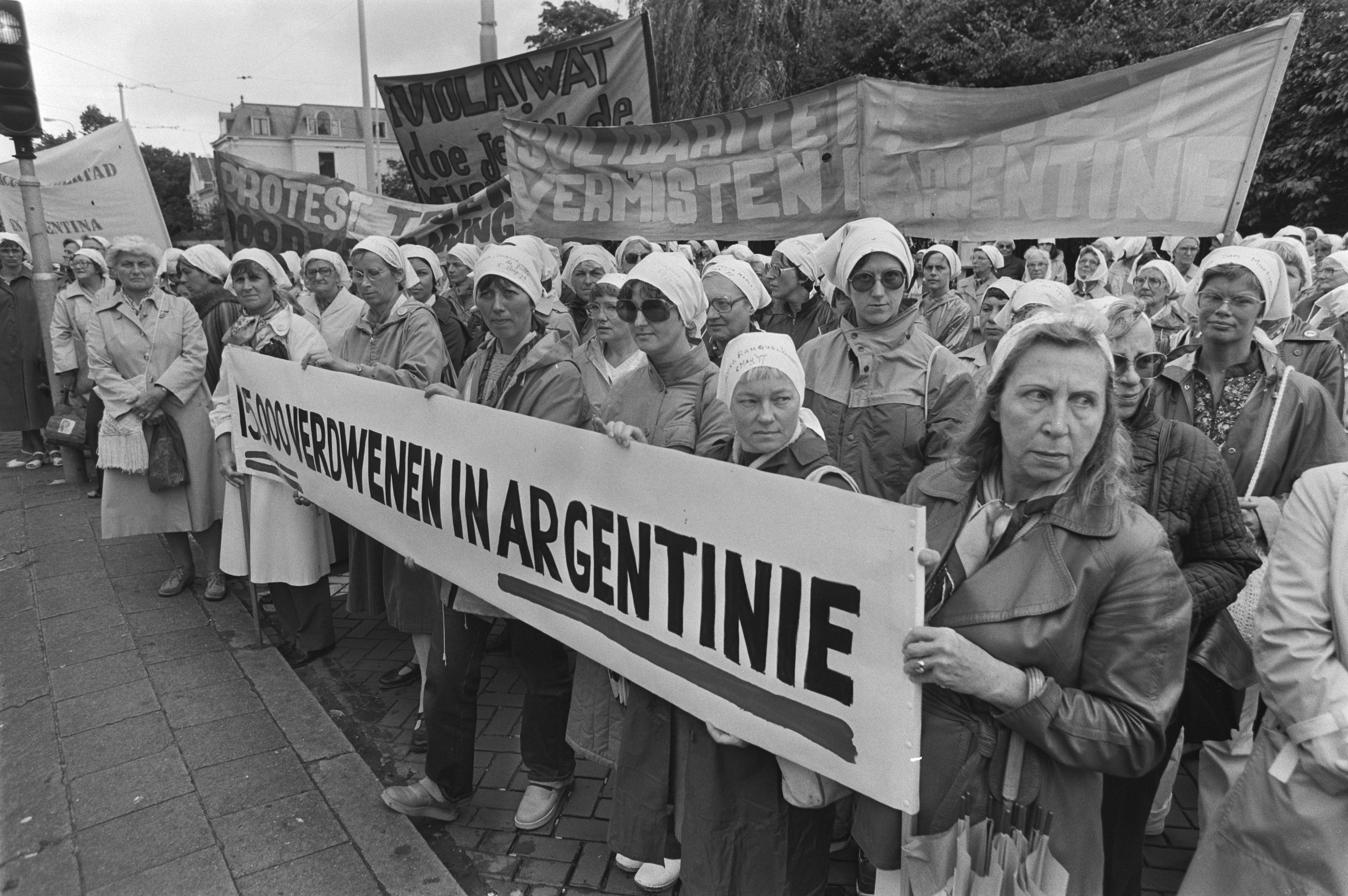 Gruppe von Frauen mit einem Banner "Argentinischer Frauenmarsch in Argentinien" vor einem Verkehrssignal, Bäumen, Gebäuden und einem bewölkten Himmel.