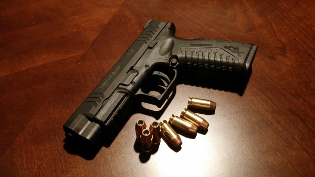 Schwarze Sig Sauer P320 X-Five Pistole mit langem Lauf und einer 9mm Magazinkapazität, präsentiert auf einem Holztisch neben mehreren Kugeln in verschiedenen Größen und Farben.