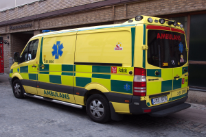 Ein Rettungswagen steht auf der Straße vor einem Backsteinbau mit Text darauf, und ein Feuerlöscher ist auf der linken Seite des Bildes zu sehen.