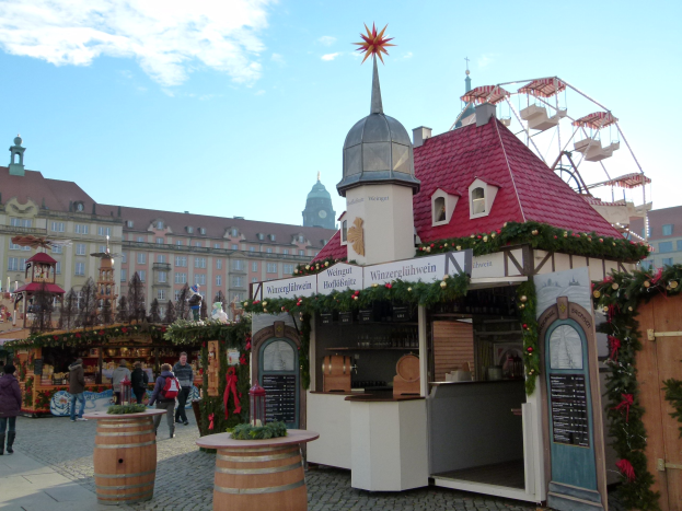 Ein geschäftiger Weihnachtsmarkt in Nürnberg, Deutschland mit Menschen um geschmückte Stände, festliche Lichter, ein Riesenrad, Gebäude und ein Schild an der rechten Seite.