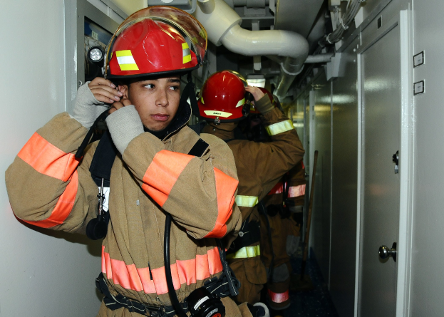 Feuerwehrleute in Uniform, die zusammenstehen und in einem Raum mit Rohren im Hintergrund während einer Übungseinheit sind.
