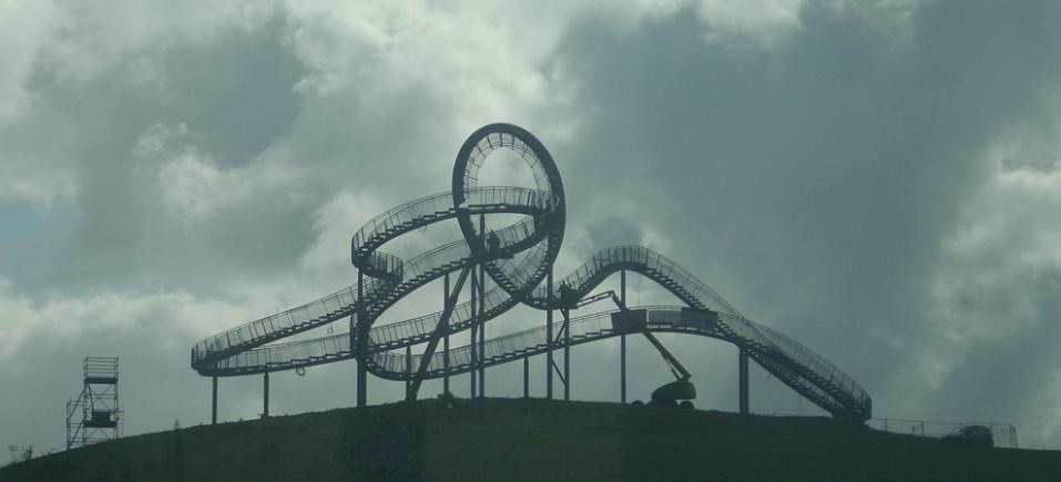 Eine Achterbahn auf dem Höhepunkt eines Hügels unter einem bewölkten Himmel, umgeben von Stützstrukturen.