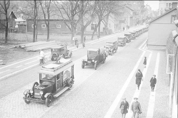 Schwarz-weiß-Fotografie aus Berlin in den 1930er-1940er Jahren mit Autos, Passanten, Gebäuden mit Fenstern, Bäumen und einem klaren Himmel.