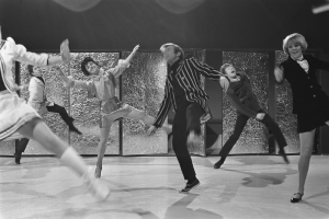 Eine Gruppe von Menschen, die auf einer Bühne tanzen, in Schwarz-Weiß, mit Schuhen und einer Wand im Hintergrund.