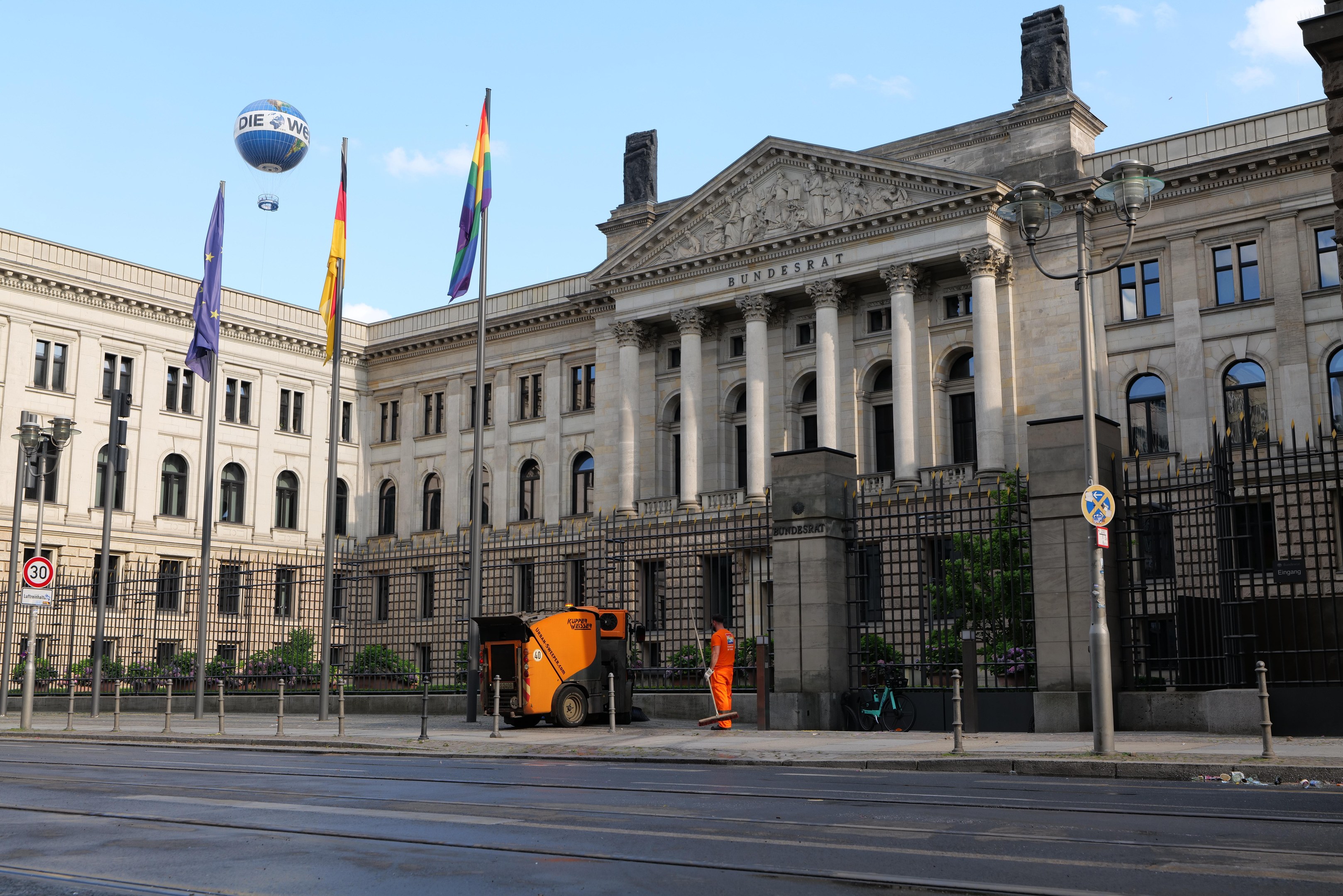Großes Gebäude mit vielen Fenstern, als Bundestag in Berlin, Deutschland identifiziert, umgeben von Straßeninfrastruktur, Fahrzeugen, Fußgängern und Bäumen unter einem bewölkten Himmel.