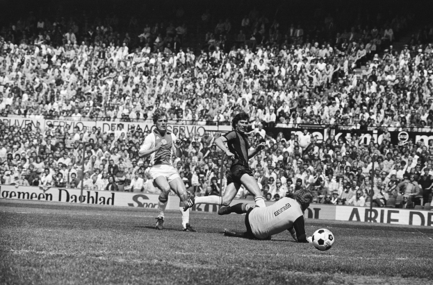 Schwarzes Foto von Männern, die auf einem Feld Fußball spielen, mit Zuschauern im Hintergrund und einer Bundesliga 1978-79 Ajax 1-1 Hannover 96-Fahne.