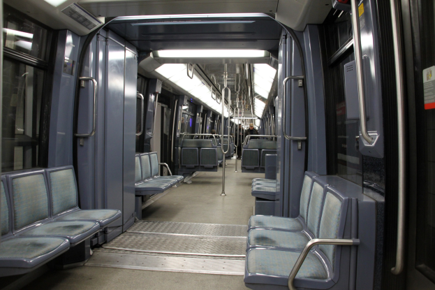 Innenseite eines U-Bahn-Zugs mit blauen Sitzen, Türen, Griffen, Stäben, Lichtern und anderen Gegenständen, mit einigen Menschen in einer belebten Stadtlandschaft.