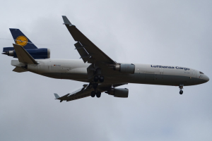 Ein Lufthansa Cargo Boeing 777-300ER im Flug, mit ausgefahrenen Tragflächen und laufenden Triebwerken, mit sichtbarem Text auf dem Rumpf gegen einen bewölkten Himmel.