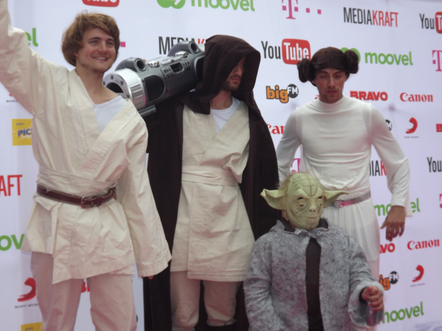 Eine Gruppe von Menschen in Star-Wars-Kostümen, die auf einem roten Teppich posieren und ein Banner im Hintergrund halten.