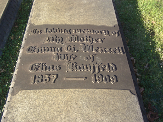 Grabstein auf einem Friedhof mit der Inschrift "In liebevoller Erinnerung an meine Mutter", umgeben von Gras und welken Blättern.