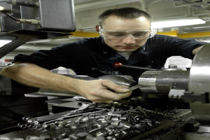 Ein Dreher trägt einen Schutzbrille und bedient eine Maschine in einer hell erleuchteten Fabrik.