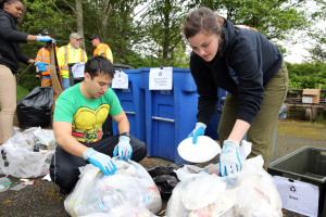 Menschen im Park Müll sammeln, einschließlich Plastik und Flaschen, mit einem Mülleimer und einer Bank im Hintergrund.