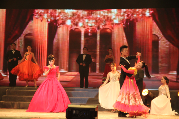 Eine Gruppe von Menschen auf einer Bühne mit Scheinwerfern, Stufen und einem Hintergrundbild, mit einem Lautsprecher unten, was eine Tanzvorstellung vermuten lässt.