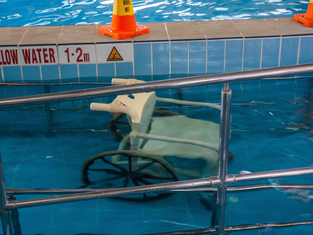 Schwimmbad mit einem Stuhl in der Mitte, umgeben von Sicherheitskegeln und einem Geländer, mit einer Wandtafel, die verfügbare Schwimmausrüstung anzeigt.