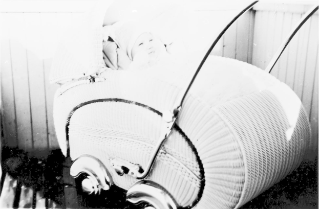 Ein Schwarz-Weiß-Foto eines Babys in einem Kinderwagen, das eine weiße Strampelhose trägt und friedlich schläft, vor einer Wand.