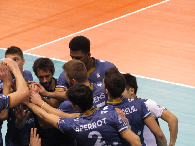 Gruppe von Männern in blauen "Ligue 1" T-Shirts, die auf einem Volleyballfeld feiern.