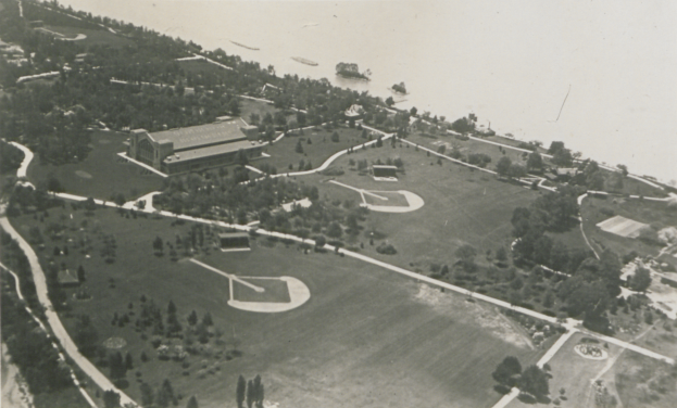 Eine Luftaufnahme eines Parks mit üppigen grünen Bäumen, hohen Gebäuden, gewundenen Straßen und ruhigem Wasser, die eine friedliche Atmosphäre schaffen.
