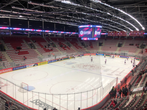 Ein Eishockeyspiel in einer großen Arena mit Zuschauern, einem Zaun um die Eisfläche, einem Display mit der Aufschrift "St. Louis Blues gegen Detroit Red Wings", Metallrahmen und einer Decke mit Leuchten.