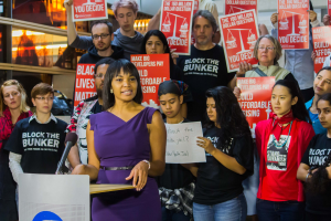 Eine Black Lives Matter-Aktivistin spricht auf einem Podium mit Mikrofon zu einer Menge mit Schildern.