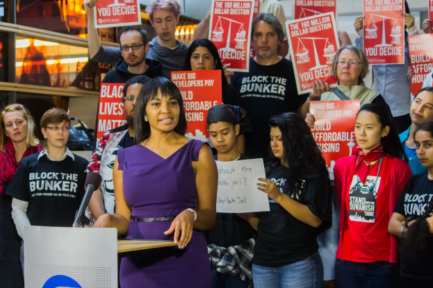 Eine Black Lives Matter-Aktivistin spricht auf einem Podium mit Mikrofon zu einer Menge mit Schildern.