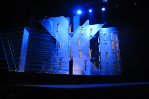 Eine Bühne für eine Preisverleihung mit dunklem Hintergrund, einigen Lichtern und ein paar Gegenständen, die mit dem Ereignis in Verbindung stehen.