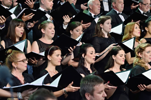 Eine Gruppe von Menschen steht vor einem Chor, jeder hält ein Buch in der Hand und singt zusammen.