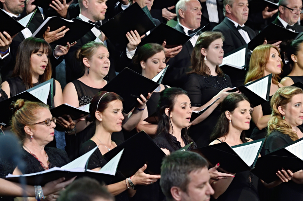 Eine Gruppe von Menschen steht vor einem Chor, jeder hält ein Buch in der Hand und singt zusammen.