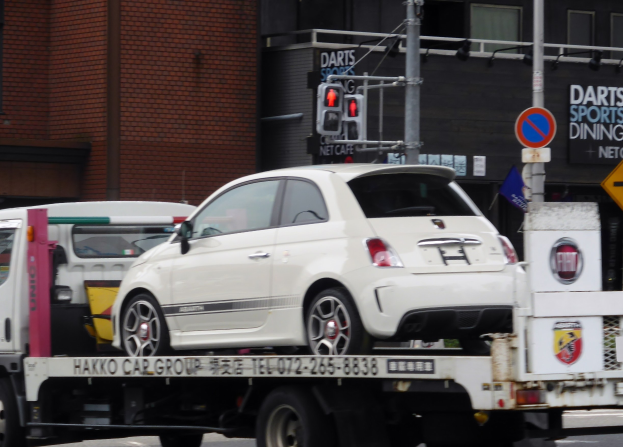 Weißer Wagen wird von einem Abschleppwagen auf einer Straße mit Gebäuden, Polen, Verkehrszeichen und Schildern im Hintergrund gezogen.